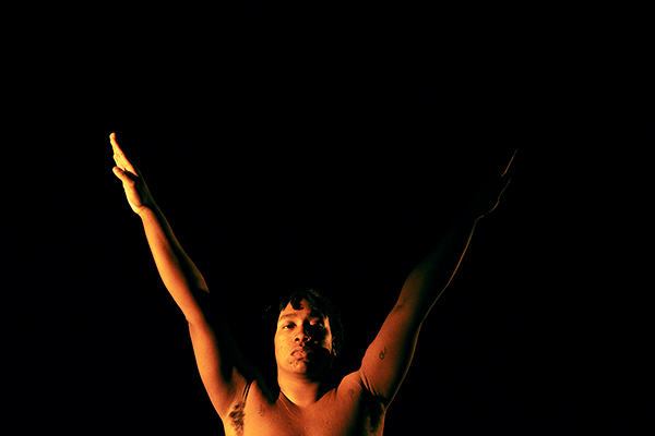 Image of Eli Mathieu-Bustos during choreography, with arms raised in a V-shape, maintaining a composed expression while facing the camera.