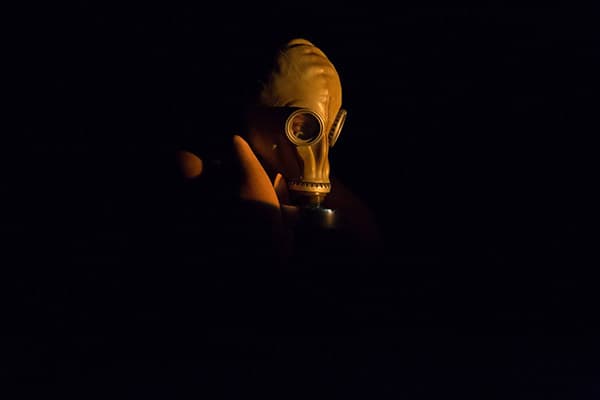 Photo of a person with gas mask and black leather apron, with free arms on the stage illuminated from above
