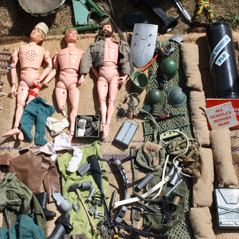 Foto am Boden verteilter Gegenstände, die zu Krieg passen dazu drei blonde Kenpuppen