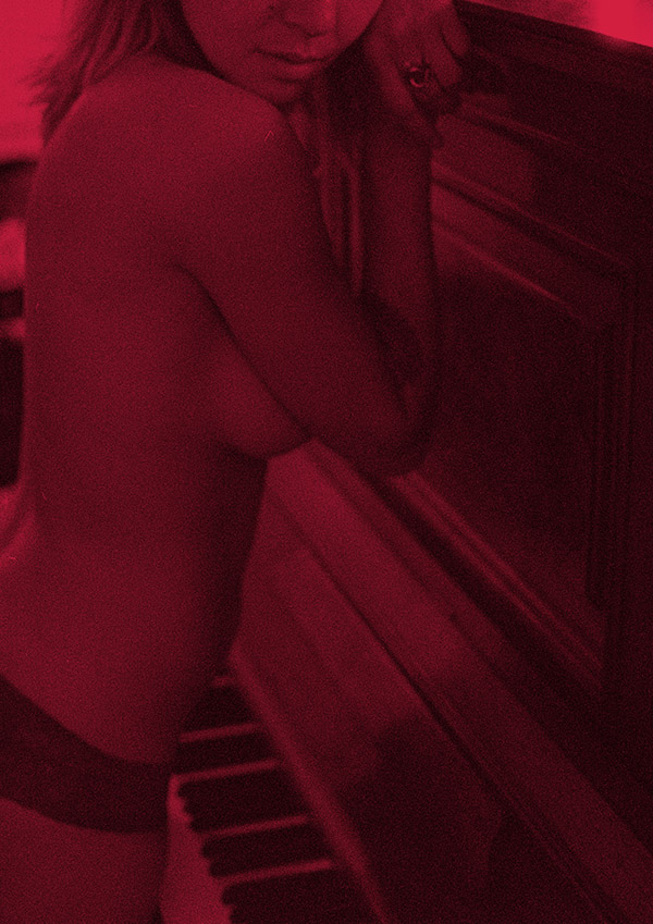 Photography of woman, dressed only in black panties standing at piano. Red filter