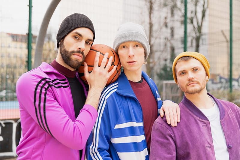 Portrait of three young men, outside, with woolen hats. A basketball between them. 