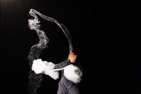 Woman dressed in black against black background playing with cotton candy