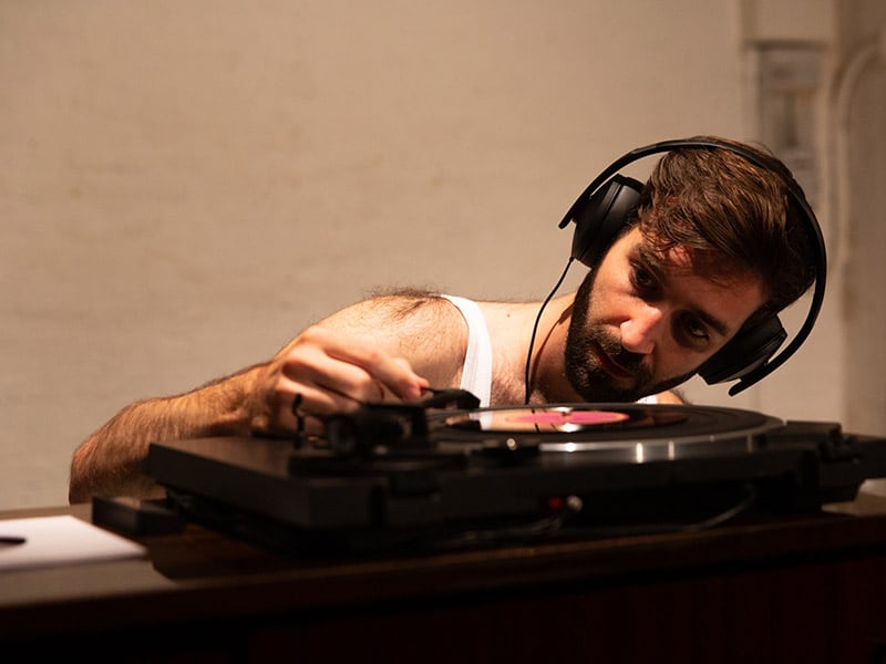 Close-up of a young man with headphones operating a vinyl record player.